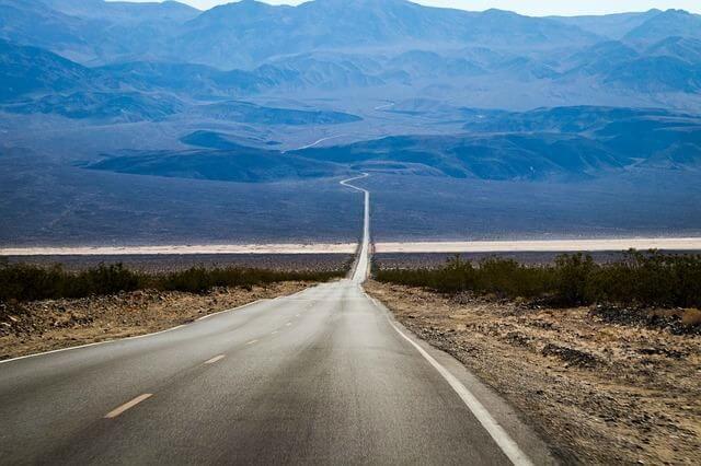 A long desert road stretching toward mountains with the quote about treating obstacles as life lessons