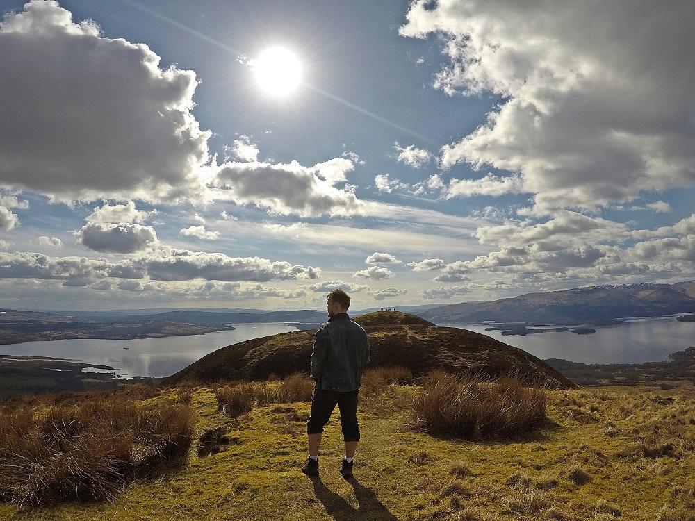 Person standing on a mountain overlooking Scottish landscape