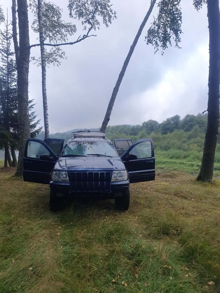Black Jeep Grand Cherokee parked among trees in a forest setting